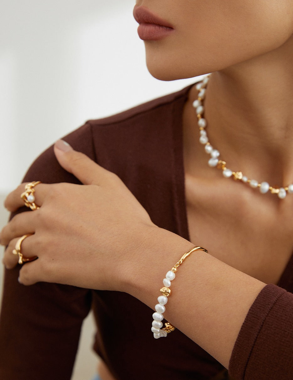 Close-up of a person wearing gold jewelry with pearls on a neutral background